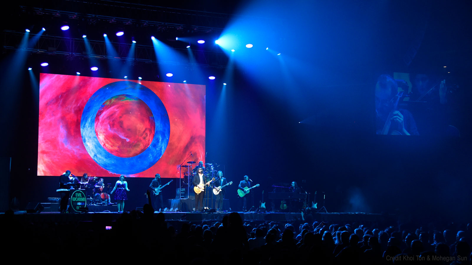 Band members of The American ELO perform in front of a giant O projection.