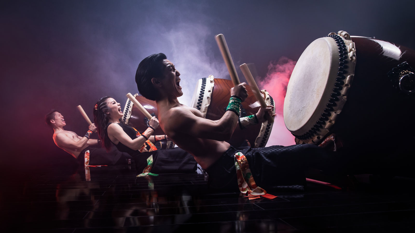 Three taiko drummers drumming together.