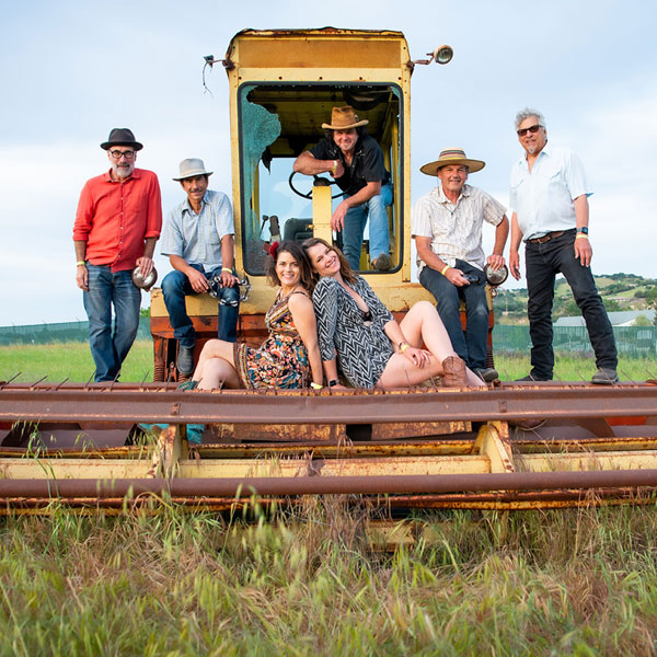 Members of Mother Corn Shuckers posed with farm equipment in a field.
