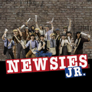 A group of news carriers with arms raised behind text of Newsies Jr.