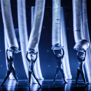 Performers dance onstage with giant aluminum tubes.