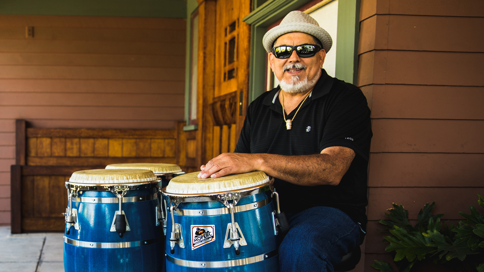 Poncho Sanchez seated on a porch with his drums.