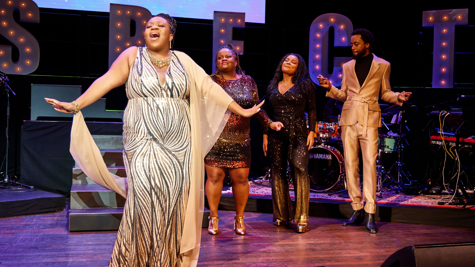 Singers performing Aretha Franklin in front of RESPECT letters.