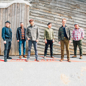 Band members of Steep Canyon Rangers standing in front of a wooden building