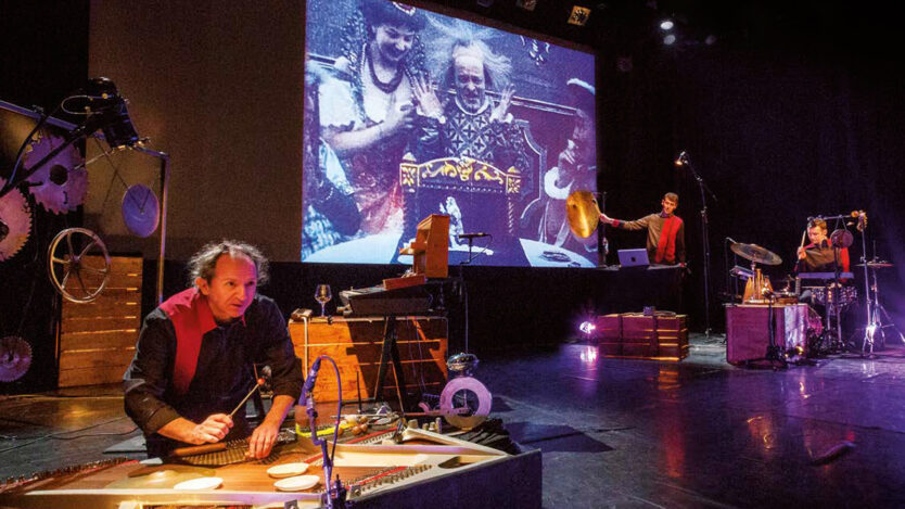 Musicians performing on stage with film playing in the background.