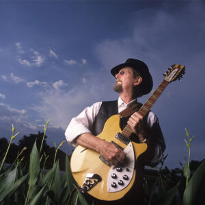 Roger McGuinn holding a guitar in a cornfield